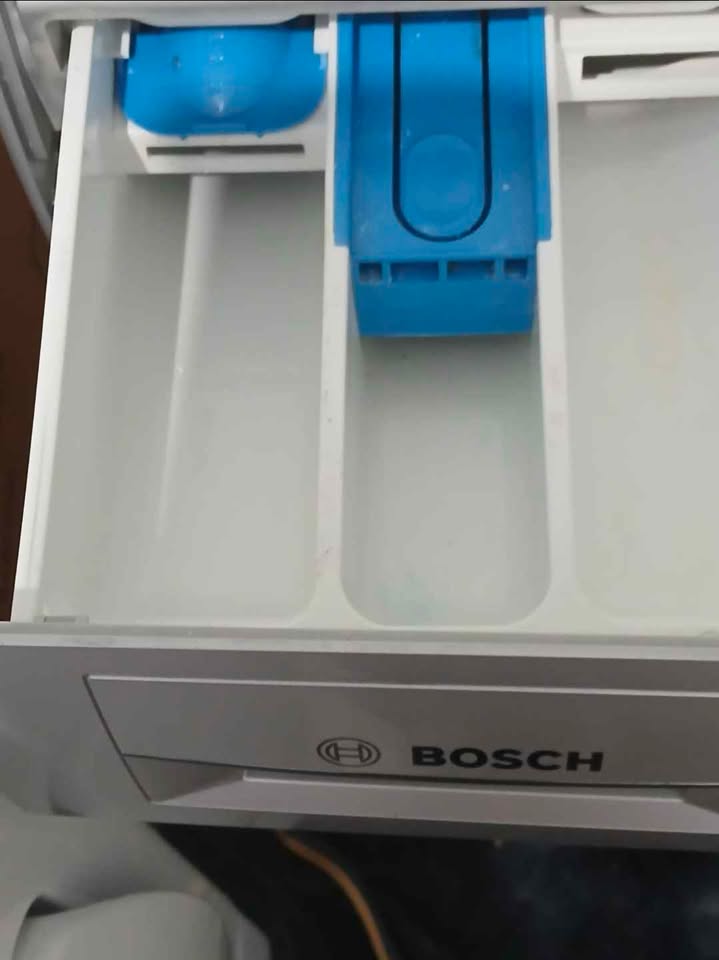 Close-up view of the open detergent drawer of a Bosch 10.5/6 KG front-load washer dryer (model WNA2E4U1IN), showing white compartments with a blue plastic dispenser insert.
