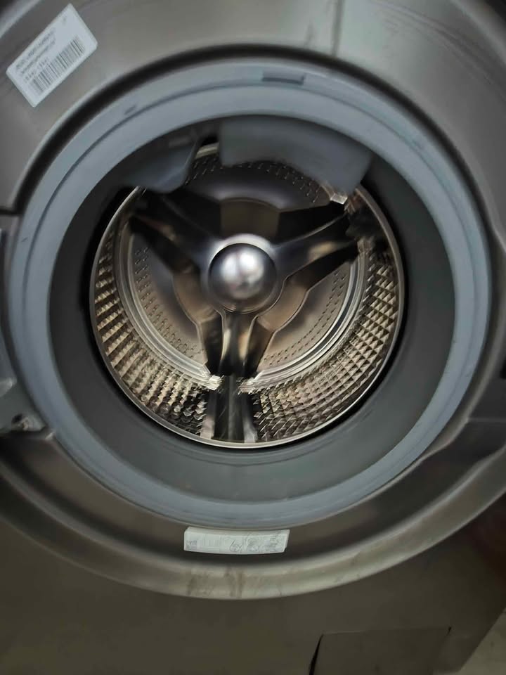 Interior view of the Samsung 12 kg wash / 7 kg dry front load washer dryer (model WD12FG5B34BBTL), showing the open door and empty stainless-steel drum with three-pronged central spindle and textured drum walls